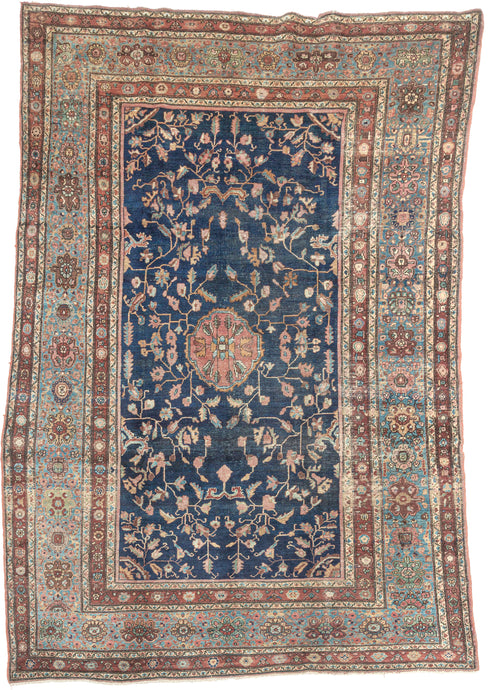 This piece showcases a graceful allover floral design anchored by a central medallion in soft rose and muted green tones. The generous borders, framed in sky blue and rust, add depth and contrast while highlighting the sophisticated floral latticework in the field. Finely woven with a dense, durable pile, this rug embodies the exceptional craftsmanship for which Sarouks are renowned