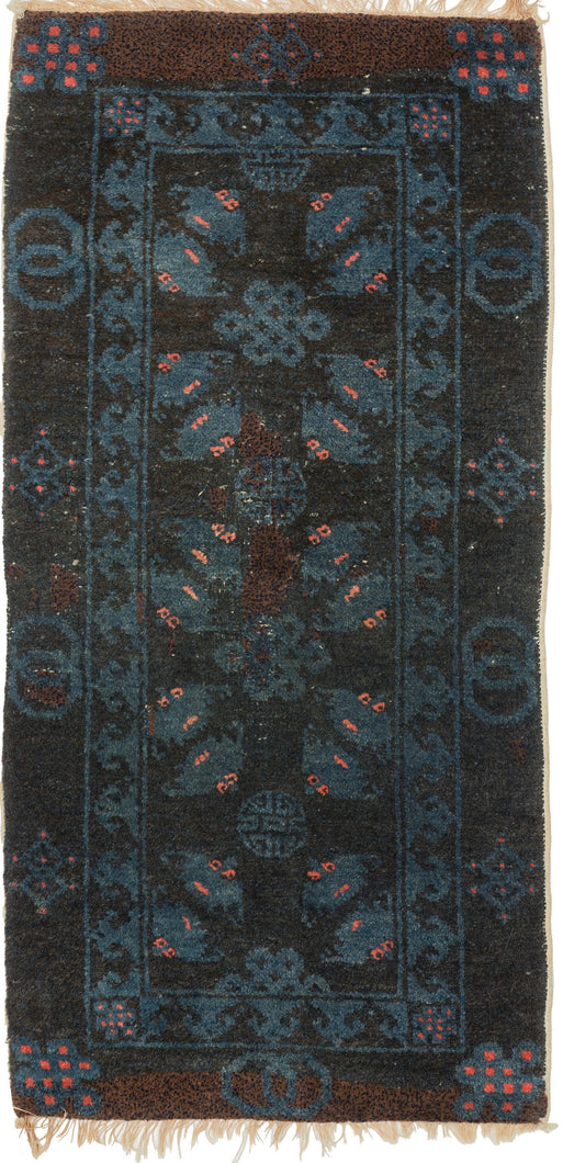 A small Gansu rug woven with a lively arrangement of auspicious symbols against a deep navy field, accented in indigo blue, coral, and muted aubergine. Pairs of stylized bats appear throughout the central field, arranged around endless knots and&nbsp;shou symbols, while interlocking ring motifs line the outer border.

In Chinese decorative arts, the bat is a symbol of good fortune, while the shou character represents longevity and the endless knot suggests continuity and enduring harmony. 