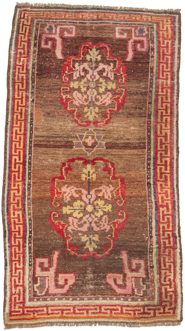 A character-rich Tibetan rug with a warm brown field and bold medallion motifs framed by a striking red key border. The saturated reds and soft pinks contrast beautifully against the earthy ground, while subtle abrash and wear create depth and texture across the surface.