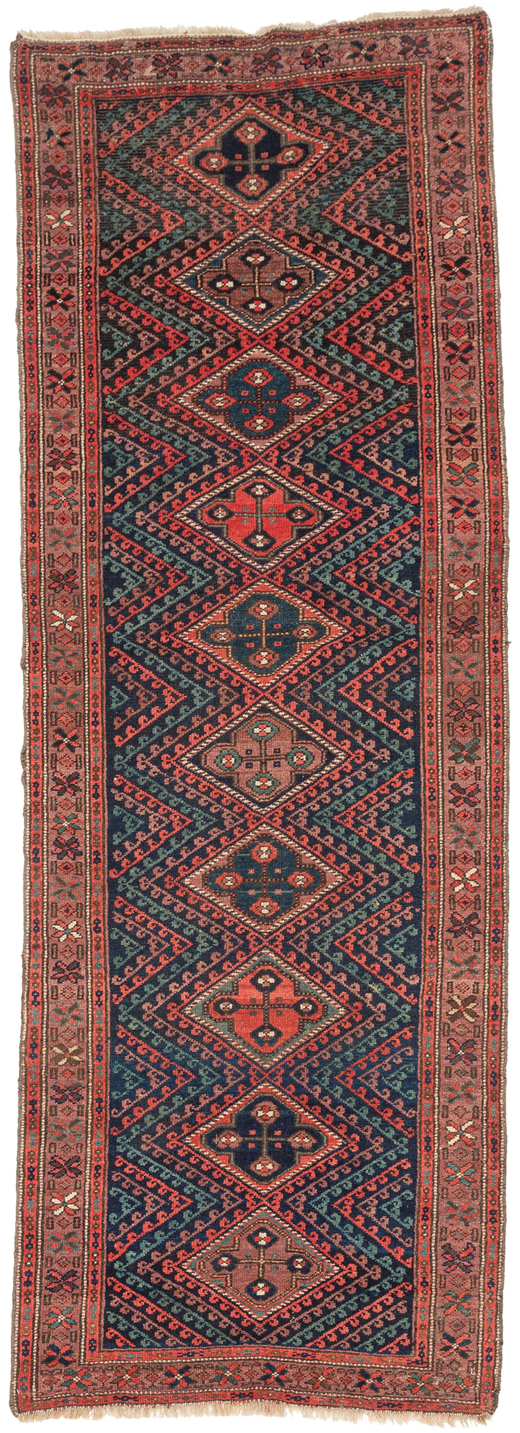 A richly colored antique Kurdish runner with a dramatic dark field and a vertical sequence of stepped diamond medallions. Each medallion contains a bold four-part floral form, set within a field of angular zigzag bands and small hooked motifs in madder red, deep indigo, soft rose, aubergine, and green.

The rug has a strong tribal character, with a narrow format, saturated color, and confident geometric drawing. The repeated diamond medallions create a clear central rhythm, while the surrounding serrated fo