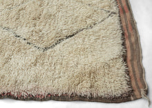This Beni Ourain rug was woven during the middle of 20th century in the Middle Atlas Mountains of Morocco.

It features a central column of black latticed diamonds on a creamy white ground.&nbsp; Red and brown stripes can be found around the perimeter, most prominently in the striped kilim end borders. Good quality wool in a large format. Often imititated this is the real deal Moroccan shag that Frank Lloyd Wright referred to as "White Giants"&nbsp;