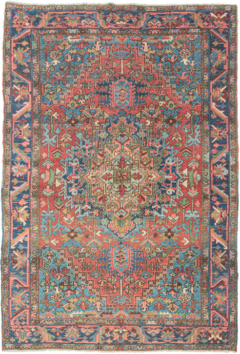 This classic Heriz features a geometric central medallion set against a richly layered field of angular vines, stylized leaves, and geometric blossoms. The palette is both vibrant and balanced with coral and madder reds forming the backdrop, while sky blue and deep indigo provide striking contrast. Soft accents of ivory, green, and gold animate the details, giving the rug a depth and luminosity.