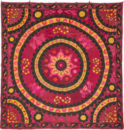 A bold and vibrant suzani centered around a large circular medallion radiating outward in layered rings of embroidery. The composition is energized by a rich crimson ground with striking accents of black, golden yellow, and hot pink, creating a dramatic and highly graphic presence.