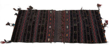 A richly textured saddle bag from Afghanistan with silky wool, woven in a dark, atmospheric palette of deep brown, black, aubergine, red, and indigo tones. The design is arranged in vertical bands with small geometric motifs, zigzag borders, diamond forms, and subtle embroidered details.