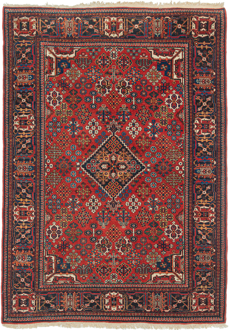 A richly patterned vintage Joshaghan rug with a dense field of highly stylized floral and geometric motifs surrounding a dark indigo diamond medallion. The saturated madder-red ground is enlivened by an unusually broad palette of indigo, sky blue, turquoise, green, ivory, apricot, gold and soft coral.