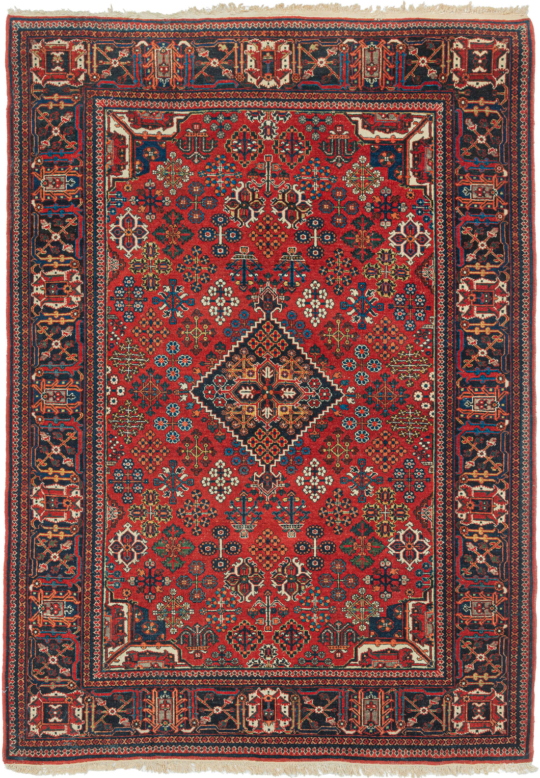 A richly patterned vintage Joshaghan rug with a dense field of highly stylized floral and geometric motifs surrounding a dark indigo diamond medallion. The saturated madder-red ground is enlivened by an unusually broad palette of indigo, sky blue, turquoise, green, ivory, apricot, gold and soft coral.