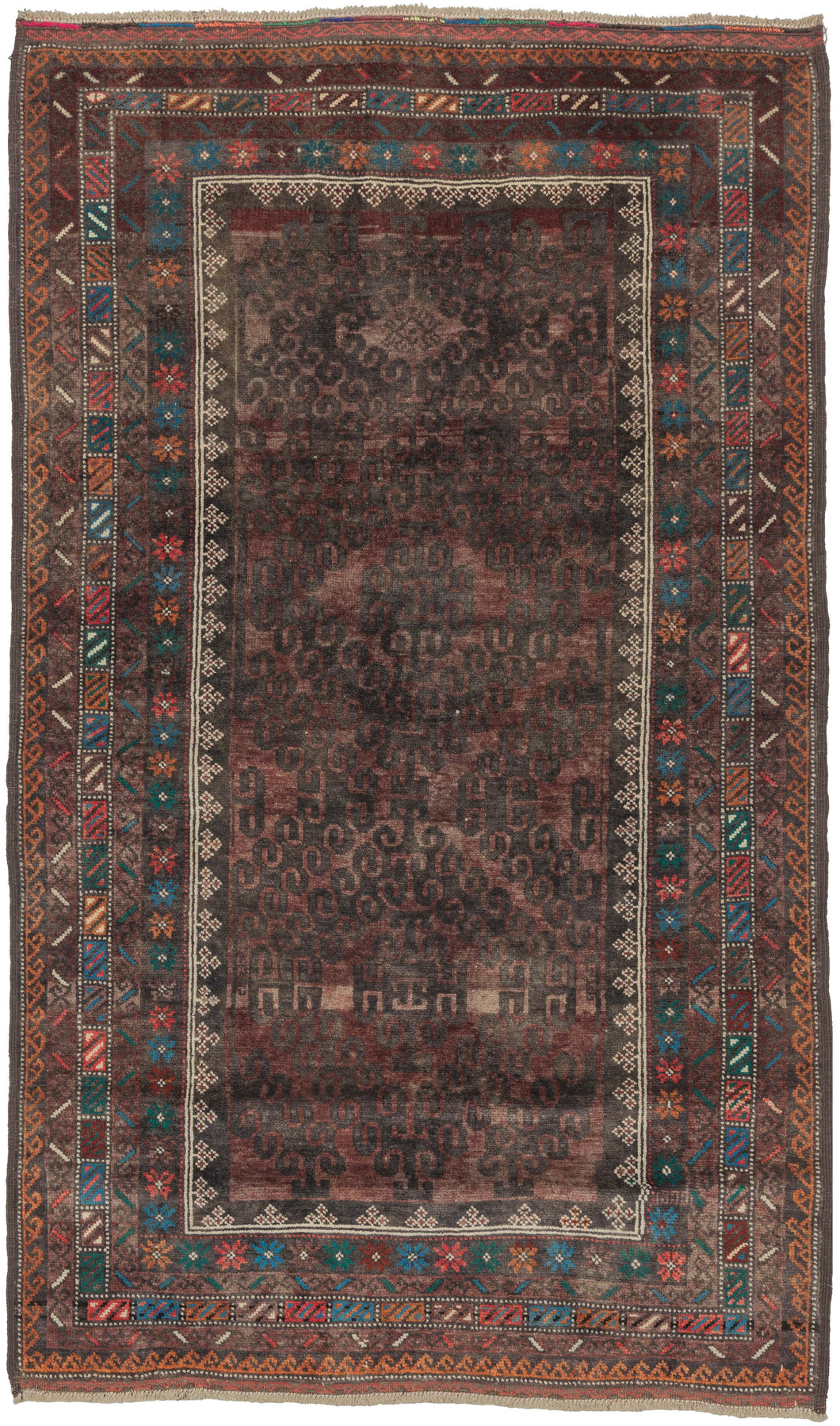 A soulful midcentury Mashwani Baluch rug with a wonderfully atmospheric palette and tribal presence. The field is built around a repeating latch-hook pattern, softened by age and wear into a smoky ground of aubergine, charcoal, madder, and faded brown. Around it, the borders bring the piece to life with small bursts of turquoise, orange, red, ivory, and green.