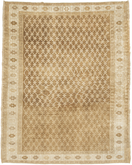 KURD Its warm camel field is animated by a playfully wonky interlocking lattice and framed by a border of larger floral medallions in soft ivory and beige. The lattice has the feel of a bent and distorted chain link fence. The delightful irregularity in the design has an endearing quality that speaks to its handmade nature and gives the piece a unique, almost whimsical character. The washed out neutral palette and subtle abrash create a natural warmth, making it a versatile choice for both traditional