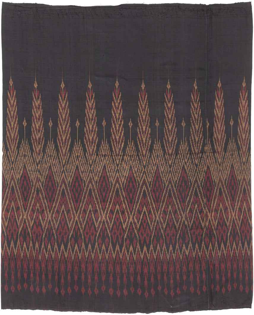 This elegant silk pha sin or traditional tube skirt was handmade northeast Thailand during the middle of the 20th century.

It is a masterful example of mudmee (ikat) weaving from the Isaan region. The central field (phuen sinh) displays alternating vertical bands of nested diamonds and stylized rice ear or flame motifs that are elongated and tapered into arrow forms that symbolize fertility, protection, and spiritual aspiration in regional Lao-Tai iconography.

The top band (hua sinh) offers a rhythm 