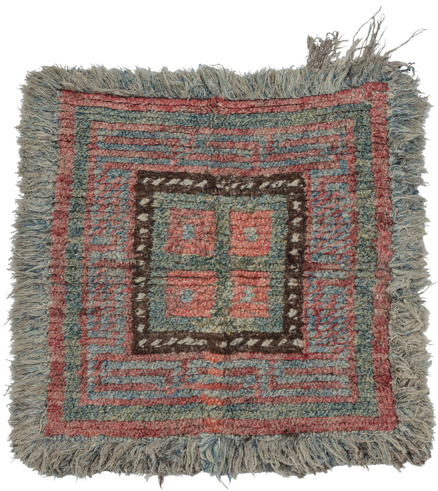 A compact Tibetan Wangden woven in the Wangden Valley of eastern Tibet, organized around a bold nested square composition. Stepped meanders radiate outward from a central panel, creating a rhythmic, architectural framework that balances symmetry with subtle irregularity. The palette of muted coral, slate blue, and mineral green is anchored by a dark brown inner border punctuated with small ivory accents.

Woven in hand-spun wool with a dense, springy pile, the piece retains its original long fringe and disp