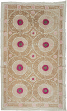 A large Central Asian suzani embroidered with eight bold medallions arranged in a balanced lattice across a warm sand-colored ground. Each circular form centers a vivid raspberry rosette with a small green center, surrounded by finely worked chain stitch that radiates outward in soft tonal rings.