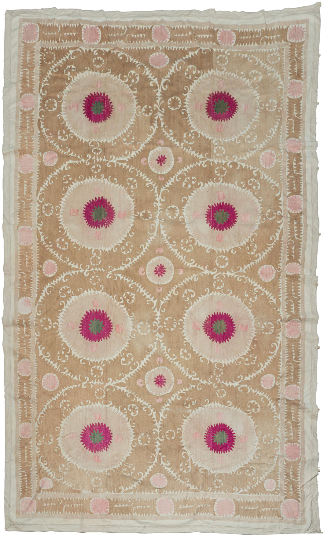 A large Central Asian suzani embroidered with eight bold medallions arranged in a balanced lattice across a warm sand-colored ground. Each circular form centers a vivid raspberry rosette with a small green center, surrounded by finely worked chain stitch that radiates outward in soft tonal rings.