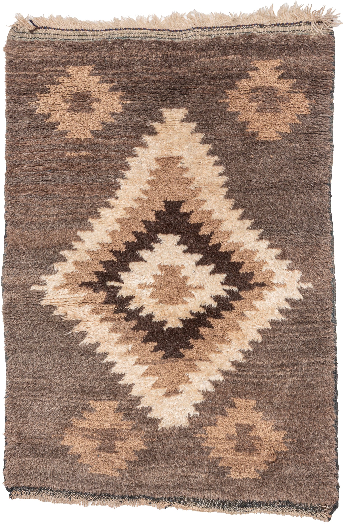 A wonderfully tactile Angora Tulu rug distinguished by its exceptionally soft, shaggy pile and striking geometric composition. Woven in a restrained palette of undyed Angora goat hair, the rug features a rich, earthy field of charcoal brown and warm taupe, punctuated by an ivory central medallion with jagged, irregular contours.