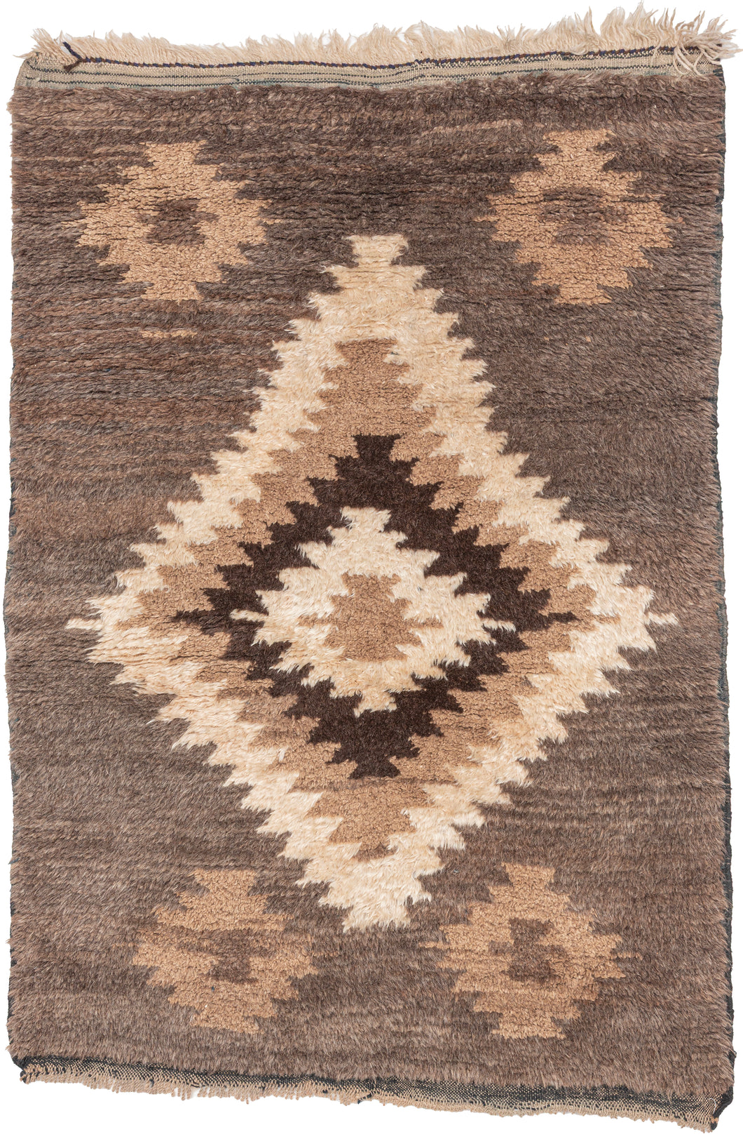 A wonderfully tactile Angora Tulu rug distinguished by its exceptionally soft, shaggy pile and striking geometric composition. Woven in a restrained palette of undyed Angora goat hair, the rug features a rich, earthy field of charcoal brown and warm taupe, punctuated by an ivory central medallion with jagged, irregular contours.