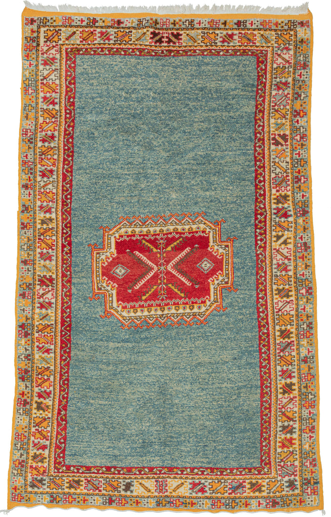 Handwoven by Amazigh weavers of the Aït Ouaouzguite tribe in Morocco’s High Atlas Mountains, this vintage rug reflects one of the region’s most celebrated weaving traditions. Distinguished by its fine weave, bold geometric design, and brilliant saffron yellow, a hallmark of Aït Ouaouzguite textiles, it embodies the vibrant artistry that has made these rugs among Morocco’s most sought-after weavings. The motifs are set against expansive fields of luminous ocean blue, whose generous negative space lends the c