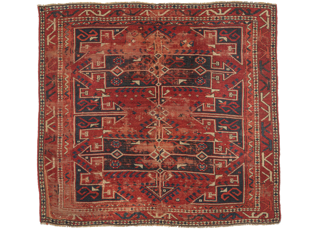This 19th Century Antique Bergama Rug features a variety of navy latch hooked cartouches in the center and geometric polygons around the perimeter against a rich red backdrop. The polygons are filled with classic tulips rendered at 45-degree angles. The rug can be read two ways with interlocking diamonds forming in the red negative space.