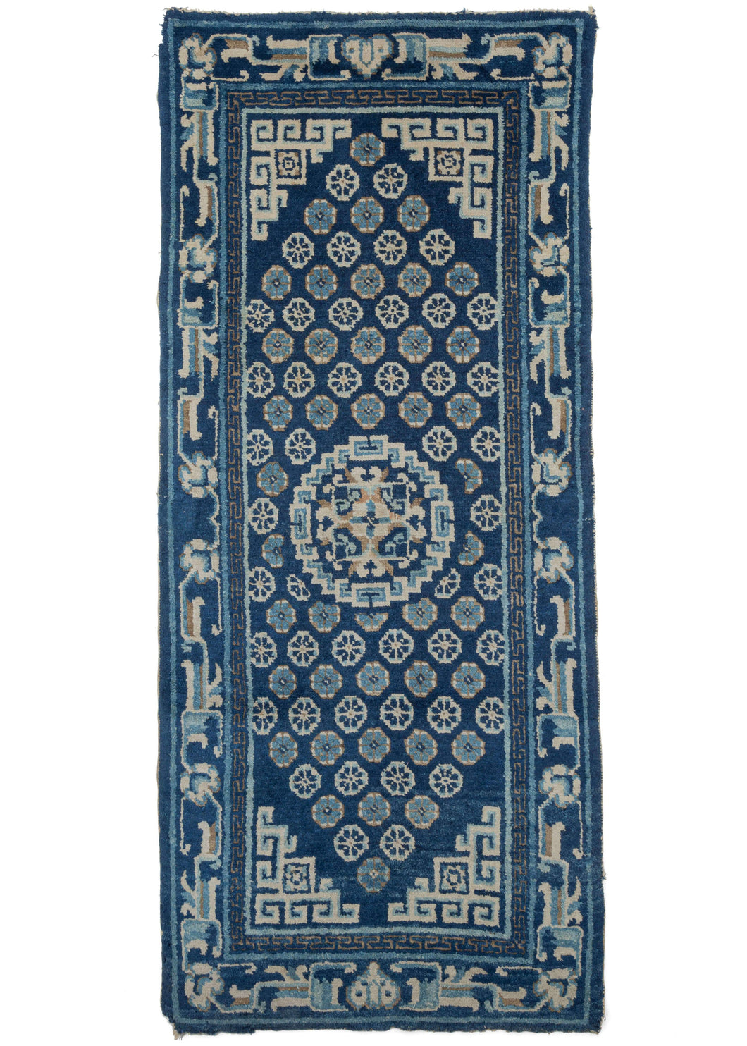 Antique Chinese Ningxia scatter rug a limited color palette in shades of blue and cream and a soft oxidized brown. The central mandala is framed by an alternating rosette pattern and scrolling cornices creating a diamond shaped field. The main border is a scrolling vine with two heart like shapes framed on the top and bottom with a minor border composed of a greek key motif.
