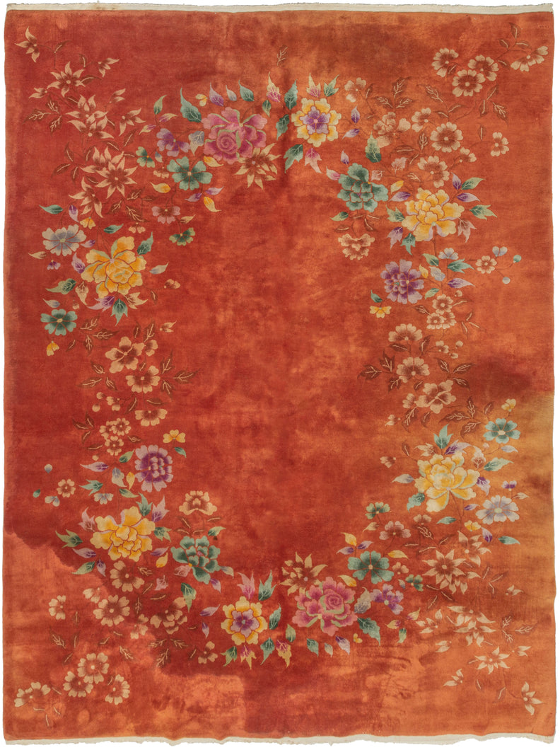 Chinese orange floral modern deco rug featuring various blossoming flowers arranged in an oval garland atop a sumptuous paprika ground. The eye-catching design features peonies, chrysanthemums, and fruit blossoms among flowers rendered in greens, yellows, pinks, and purples that really pop. 
