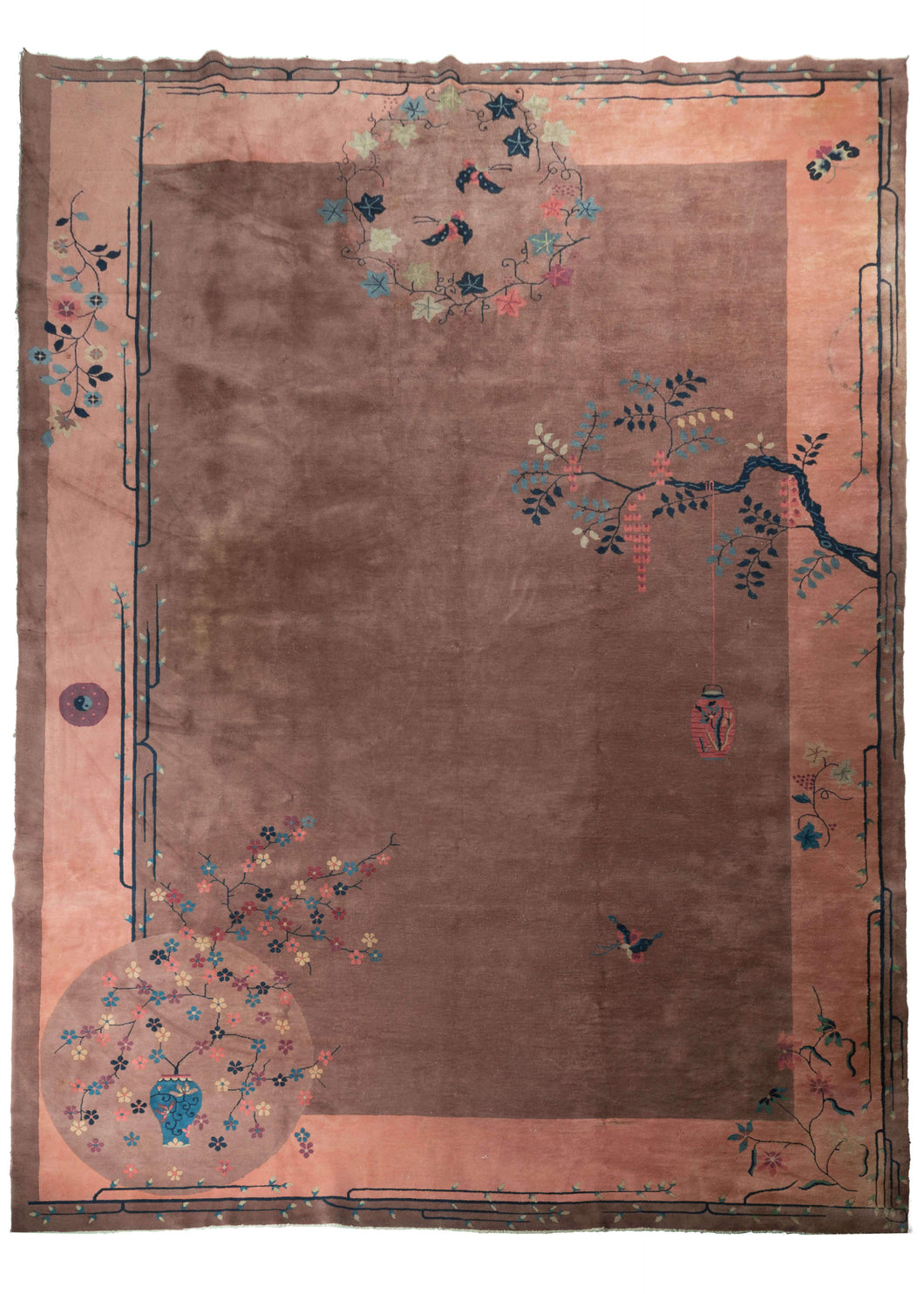Chinese Deco rug that features a calm mauve ground with a soft coral border. The design is directional and whimsical which is not restrained by the border. In the bottom left is an orb containing a vase with branches full of multicolor rosettes. A flowering branch grows form the right side with a hanging lantern. A single, small yin-yang symbol is seen in the border on the left hand side.