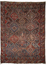 Antique Khamseh rug that features two rows of interlocking polygons on a field that shifts from deep navy to mallard blue. Both the field and the polygons are chock filled with a variety of flora and fauna from shrubs and rosettes to birds, dogs and abstracted mythological creatures. The perimeter is composed of stepped pyramids and other architectural elements which jut into the field. 