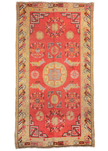 Antique Central Asian Khotan rug featuring a grayish purple and yellow central medallion surrounded by butterflies and medallions atop a dramatic red field. It showcases classic Khotan patterning which is a wonderful hybrid of both Western and Eastern Asian design elements like the lattice cornices, tri-color cloud band outer border, and greek-key interior border. 