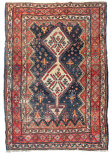 Antique south Persian Lori rug featuring two ivory lozenges topped a directional "arrow" top on a navy ground. Each lozenge contains serrated leaves and other devices in blue, red, and purple. The scalloped edge field is full of various botehs, rosettes, and what could be described as either tree of torches in soft blue and an energetic yellow. The whole is framed by a red main border that contains the same devices as the ivory lozenges and two minor borders in the same bright ivory tone.
