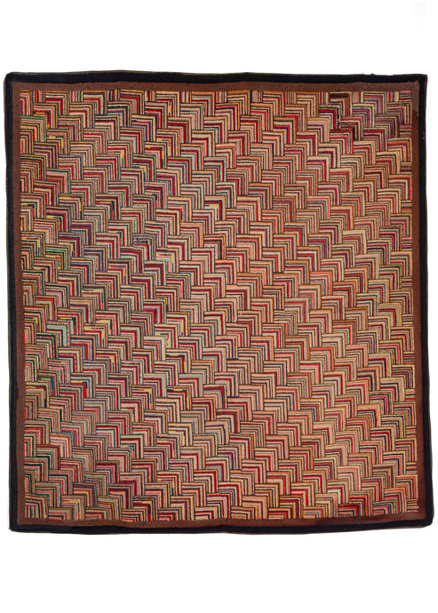 Antique North American square hook rug featuring a multicolored color palette, with an overall warm tone. The pattern is a variation of the classic log cabin design rendered in a way which it is reminiscent of the scales of a fish and that gives the piece added dimensionality. A thin dark brown border frames the whole. 