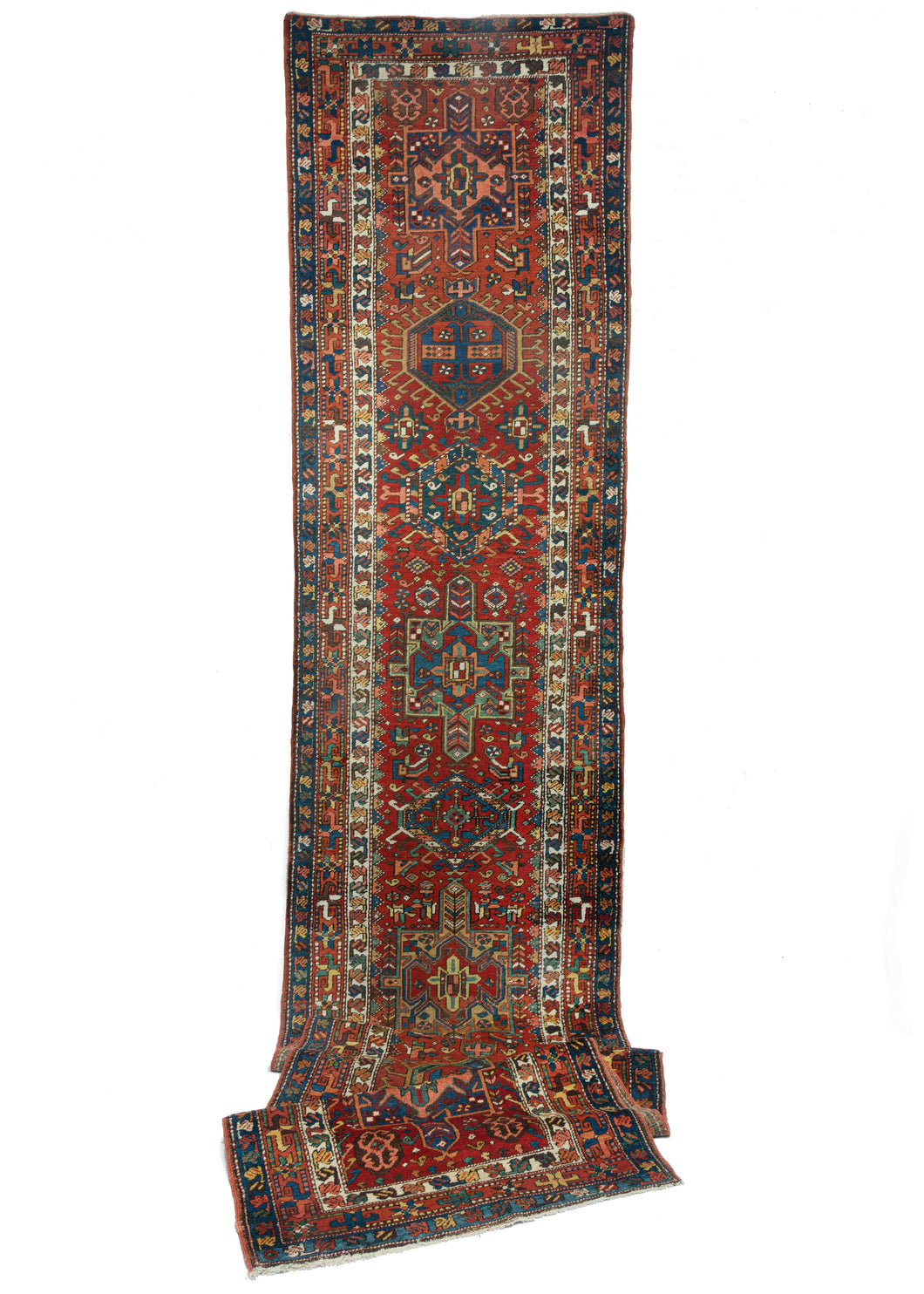 Antique NW Persian Karadja runner featuring a pattern of alternating geometric shapes and hooked lozenges on a beautiful brick-colored field. A cheerful range of Indigo blues, sage green, corals, yellow and purple interact beautifully while an ivory tone both frames the field and provides bright pops of cool white.