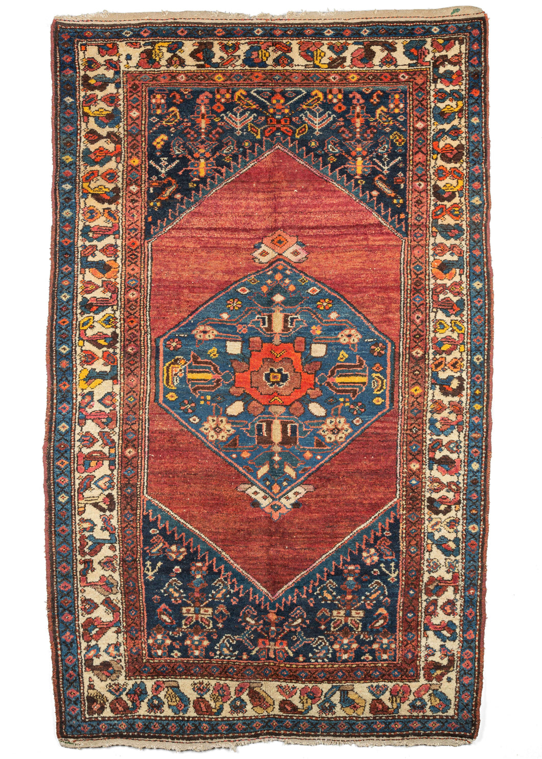 Antique NW Persian Hamadan scatter rug featurinng a pulsating red field between an indigo central medallion and cornices and contains three distinct borders in red, ivory, and blue. The reds on this rug have been “painted” over using fountain pens and ink, a practice common during the 1920s and often associated with Sarouk rugs of the period.