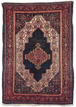 Antique NW Persian Senneh area rug featuring a deep inky blue field with a central medallion. Framing it is an ivory band filled with a twist on the classic Herati pattern, which is continued in the inky blue cornices. The minor border is composed of a simple small-scale diamond pattern, while the main border contains two patterns: the top and bottom has a diamond pattern, while the left and right sides have an a pattern of alternating palmettes.