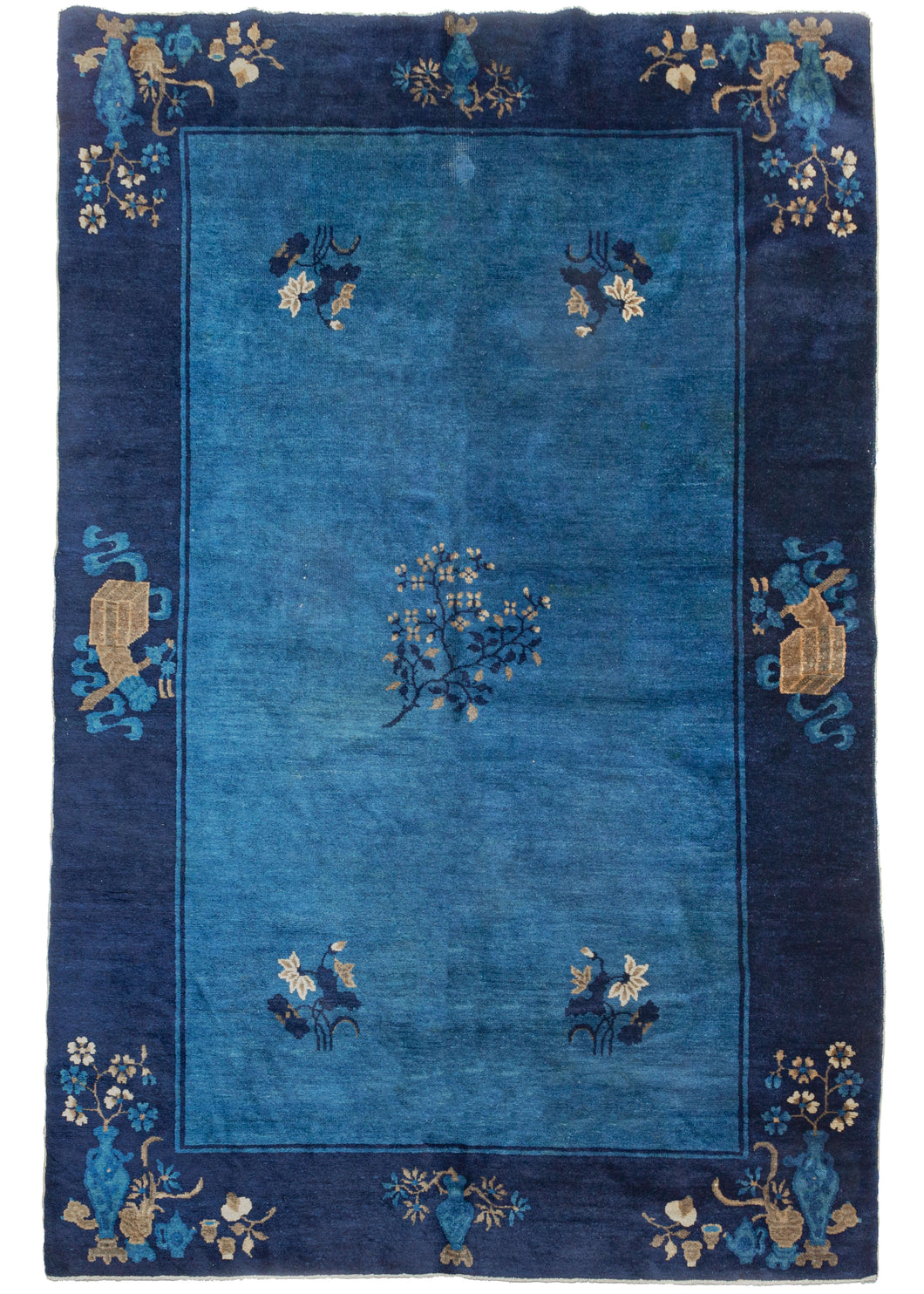 Antique Peking rug featuring a sparsely decorated light blue field with single blossoming branch in the center flanked by a grouping of various flowers in each corner.  The whole is framed a navy border featuring vases and tea sets and auspicious symbols surrounded by bent ribbons.