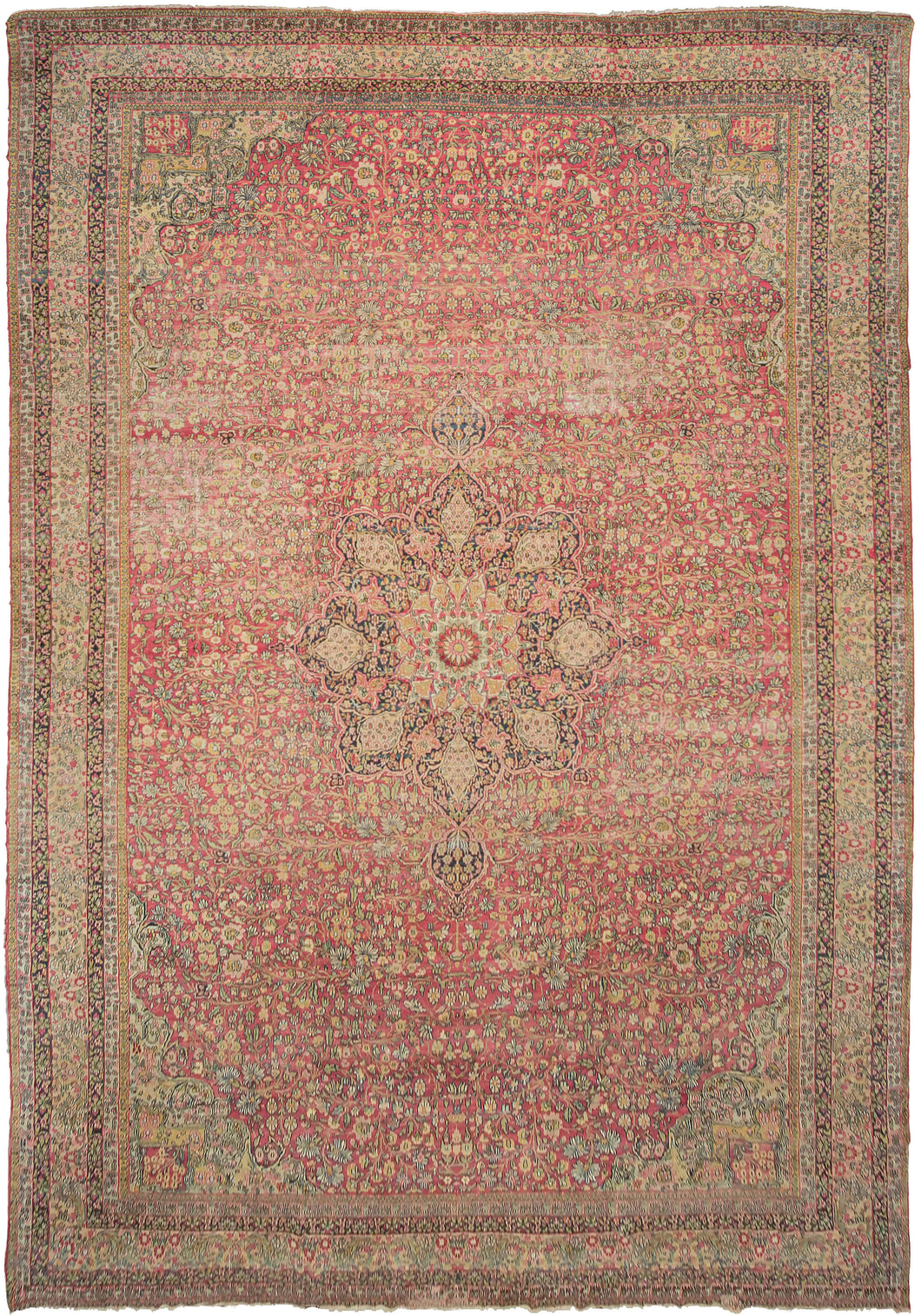 This Lavar Kerman rug was handwoven during latte 19th century in Central Iran.  This oversized rug features a central medallion with a curvilinear floral design and scalloped cornices. The cornices are distinct but have a continuous feel with the central medallion. The field features a vast array of blossoming flowers on patinated fuschia ground.  Tones of yellow, golden wheat, chartreuse, coral and ivory round out the gentle and nuanced palette. 