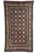 Antique Tibetan Meditation mat woven in Gansu featuring a repeating floral trellis design in brown, blue, yellow, and pink with a geometric main border. The fringe runs across the length, suggesting this rug was woven horizontally.