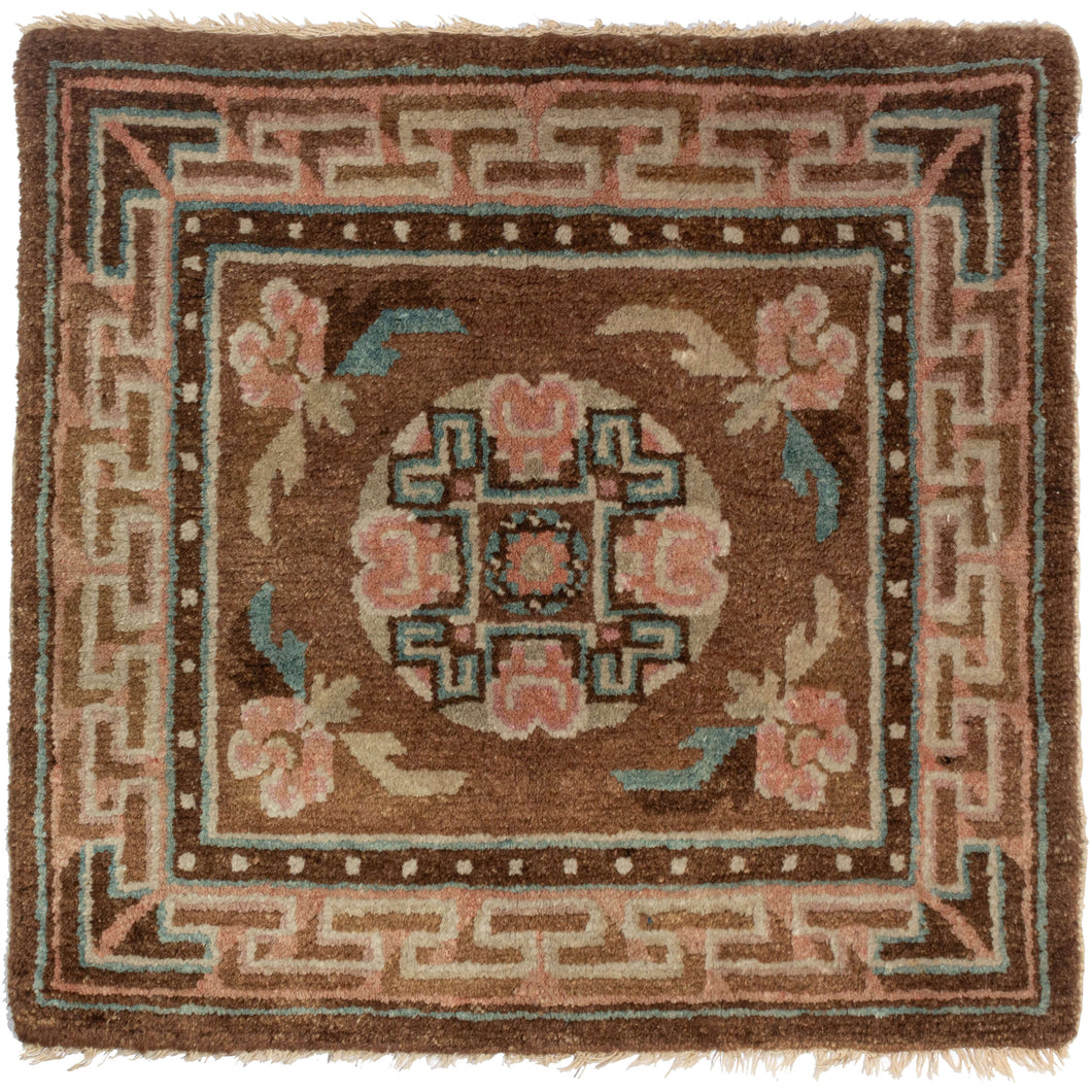 Antique Tibetan Meditation Mat featuring a simple design of a central mandala flanked by four flowers woven in blue, pink, and cream on a brown field. A highly dimensional fret border appears to float around the perimeter.