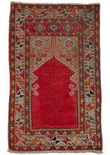Antique Turkish Karaman prayer rug featuring a bright red mihrab (prayer niche) on a camel ground. The largely geometric details are rendered in brown, purple, orange, yellow, and black, with the tricolor selvedge bringing it all together.