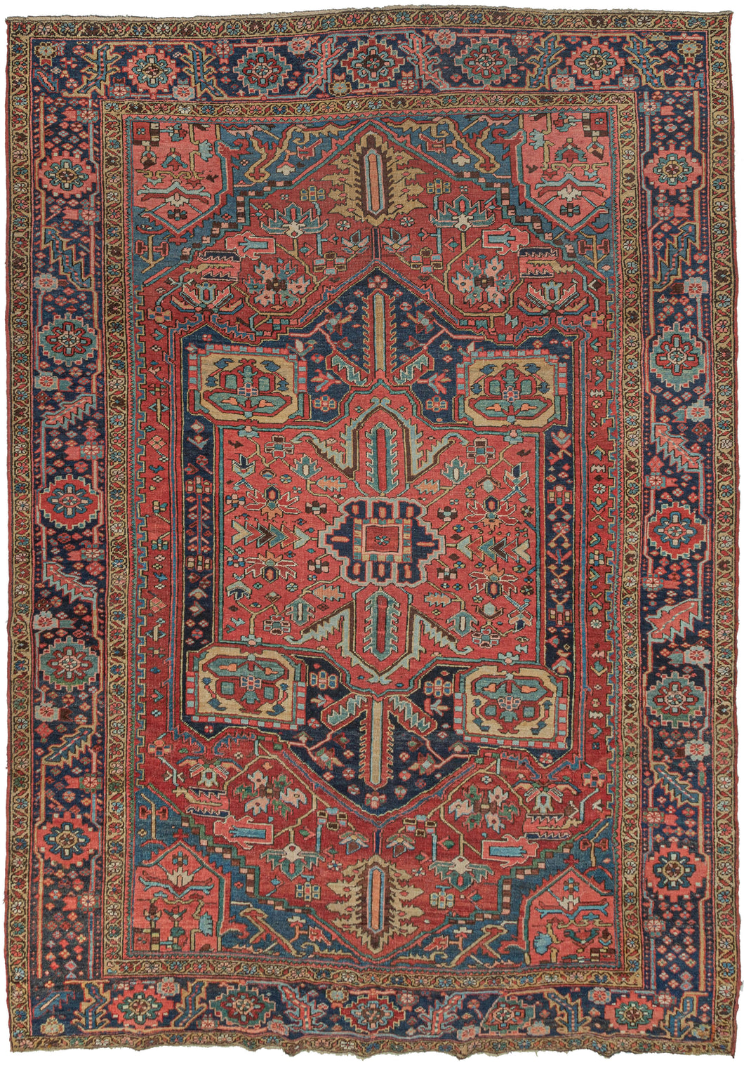Antique roomsize Heriz rug featuring a geometric central medallion on a madder red ground. The design of the more boxy medallion throughout completely changes the composition giving this piece a unique feel. Soft pinks and gold work well with jewel-toned blues and greens that really sing. Framed by a main border of rosettes and serrated leaves, the border pattern breaks near the bottom edge on both sides where the weaver filled the space with various small rosettes like a patch of wildflowers.