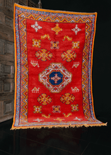 Moroccan rug handwoven during the mid 20th century. Minimal design paired with bold color palette. Bright red field contains a central medallion with smaller shapes and animals. Orange, yellow and ivory. 