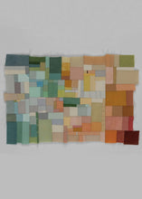 Erin Wilson quilt entitled Assembly 17 featuring a bright and colorful palette that ranges from blues, greens and yellows to oranges, red and maroon. This range of color extends from the left to the right, with sections of ivory dispersed throughout to add a lightness to the piece. The outer shape of this piece is asymmetrical and features raw edges. 