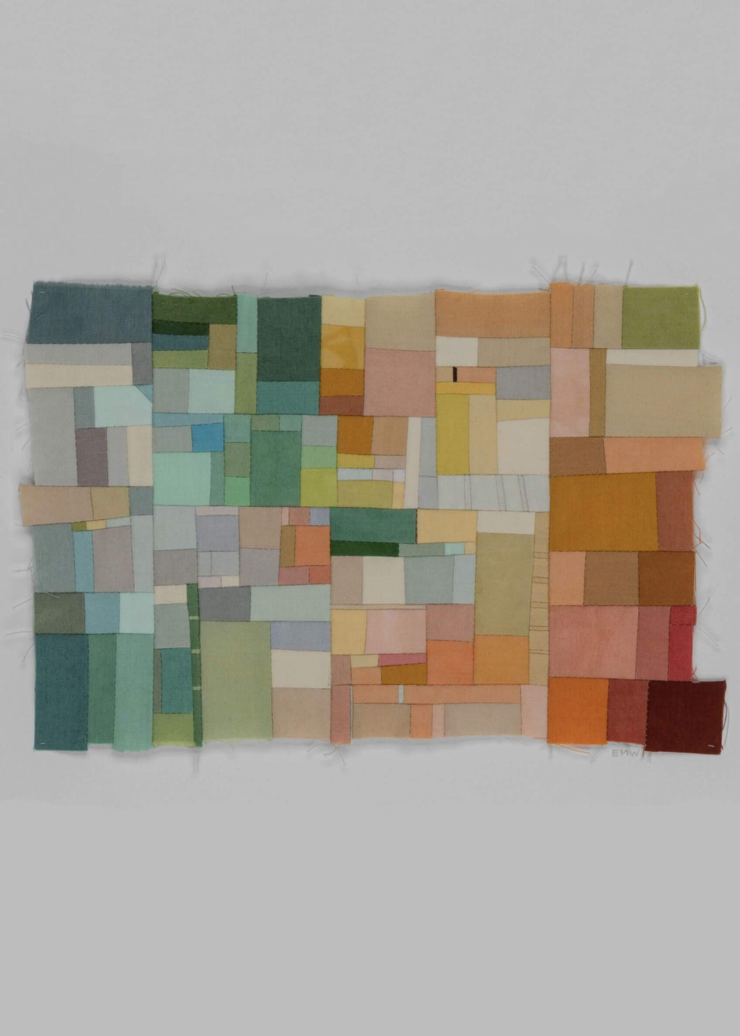 Erin Wilson quilt entitled Assembly 17 featuring a bright and colorful palette that ranges from blues, greens and yellows to oranges, red and maroon. This range of color extends from the left to the right, with sections of ivory dispersed throughout to add a lightness to the piece. The outer shape of this piece is asymmetrical and features raw edges. 