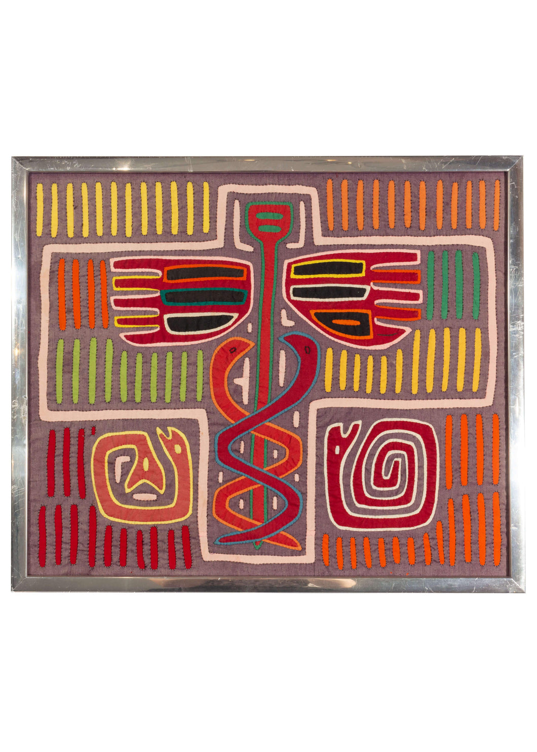 Framed Kuna Mola Cloth featuring vibrant yet faded tones of purple, green, red, orange, yellow and blue. A central cross features interlocking snakes climbing a pole. The left base features a two headed snake and the left base a snake in pinwheel form. Vertical lines in different colors add interest and excitement to the piece. It has been framed in an aluminum frame some years ago. 