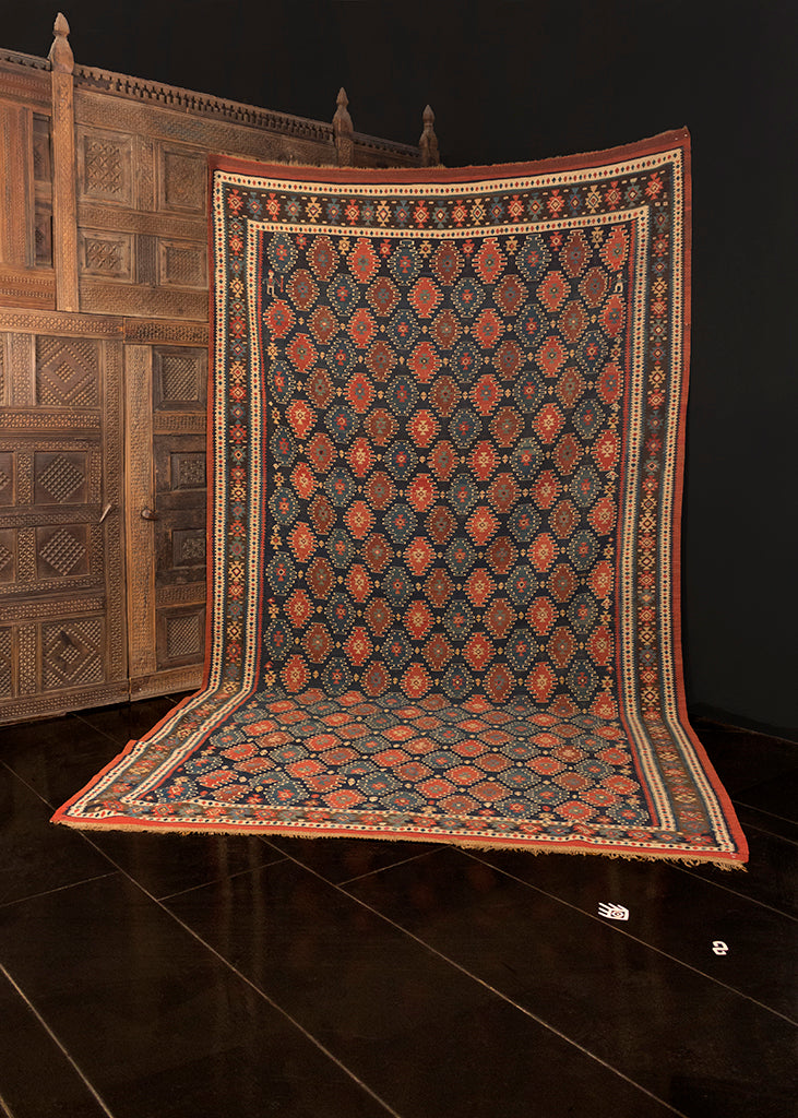 Fine kilim handwoven during early 20th century in Northwest Iran. Small diamond motifs in red and light blue, each outlined in an ivory wavy line. Two hookah smokers in the top corners. Ground is deep blue with borders in ivory and blue. 
