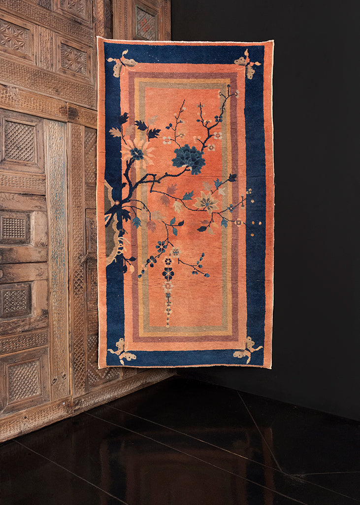 Deco rug handwoven in second quarter of 20th century in Beijing area of China. Peach pink ground with multiple solid borders in indigo, green and yellow. Whimsical with four butterflies, cherry blossom branch growing from one edge. 
