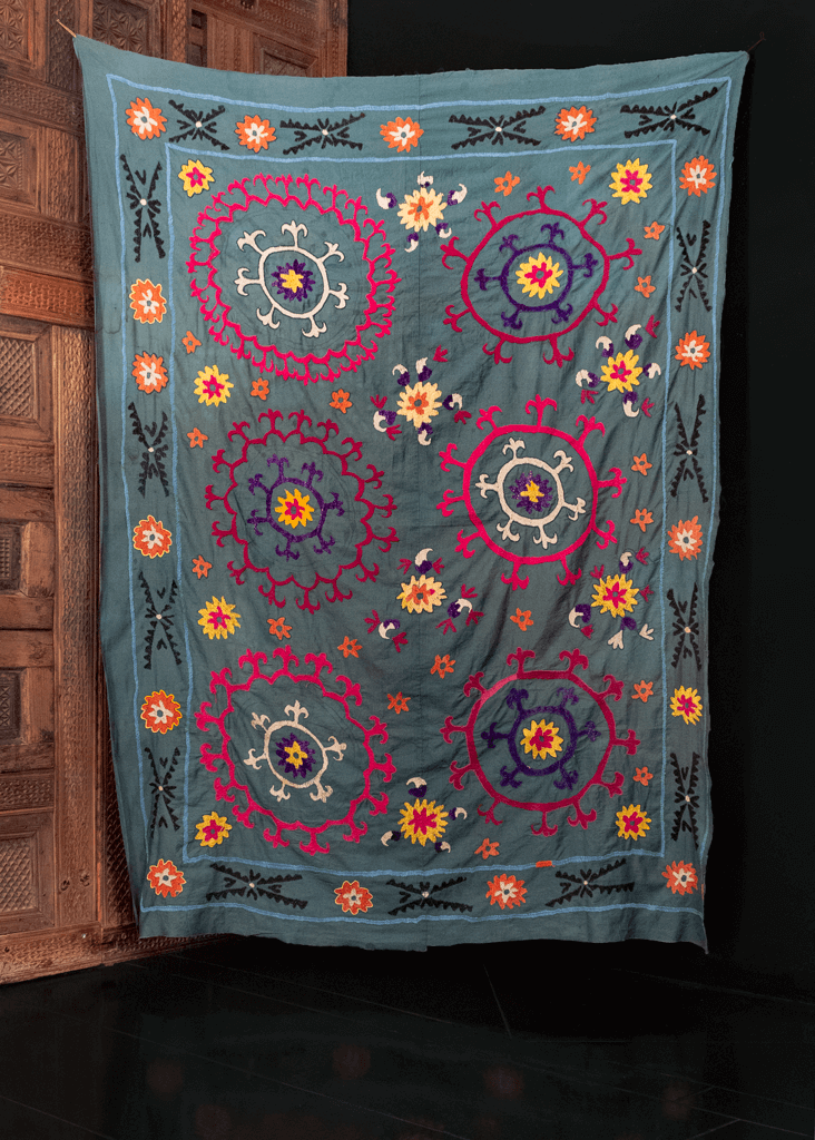Suzani handmade in Uzbekistan during fourth quarter of 20th century. Six circular medallions in pink, purple, and blue atop slate ground. 