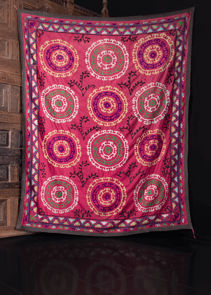 Suzani handmade in Uzbekistan during third quarter of 20th century. Repetitive design of circular medallions in purple, yellow and green atop a magenta ground. 