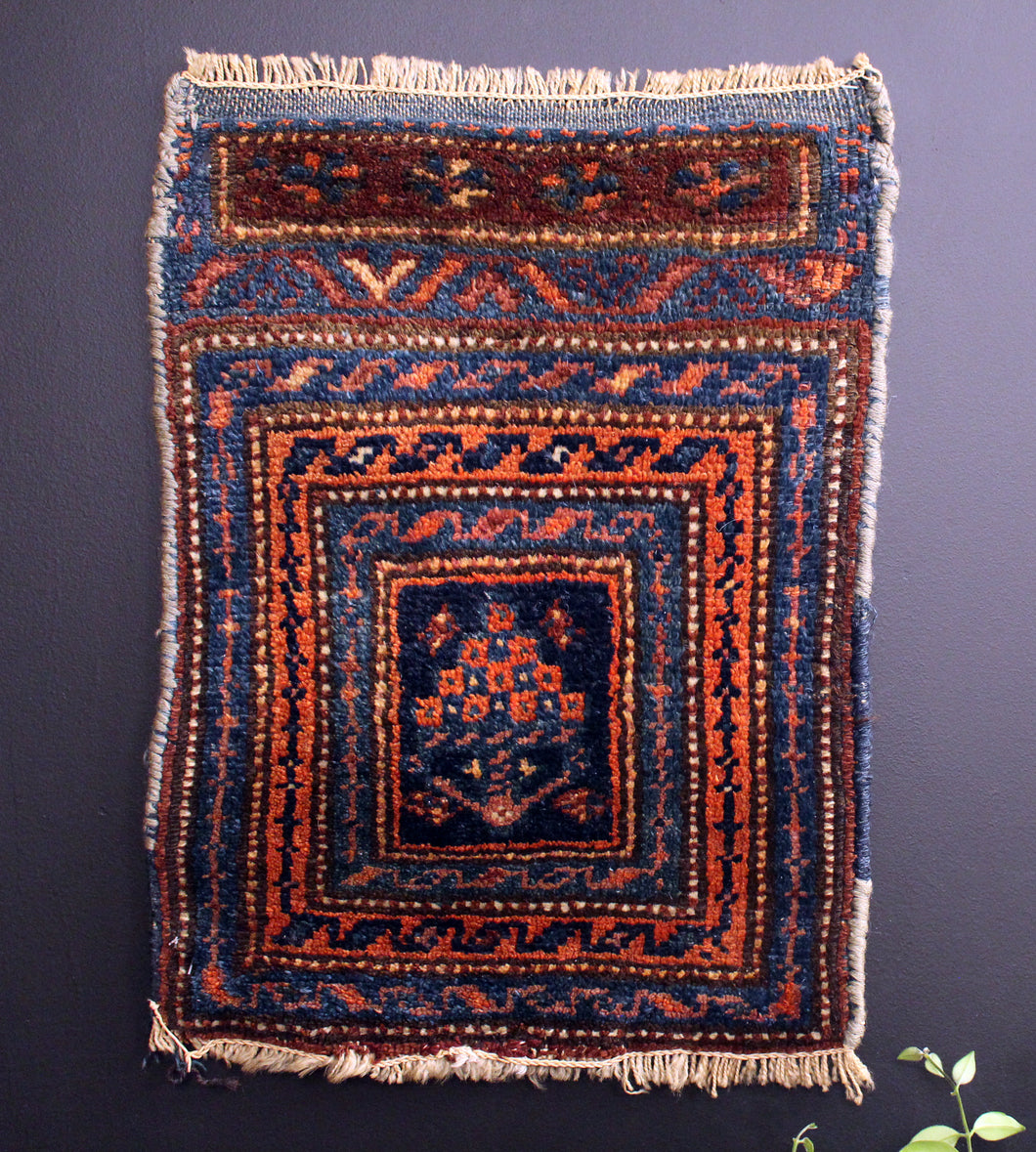 Small Kurdish rug with concentric borders that frame a bouquet of stylized flowers. Blues, oranges and reds. 