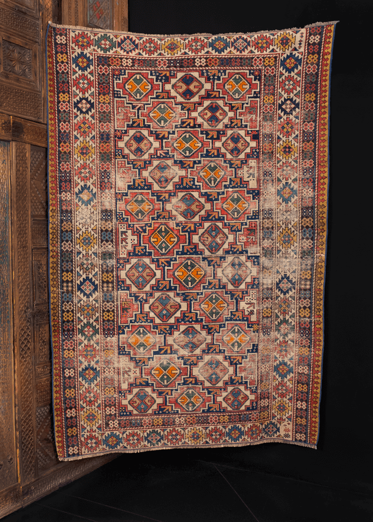 Shirvan rug handwoven in Caucasus turn of the 20th century. Geometric design of small medallions in diagonal columns surrounded by ivory border. Reds, greens, orange and blues contrasted with cream and brown wool. 