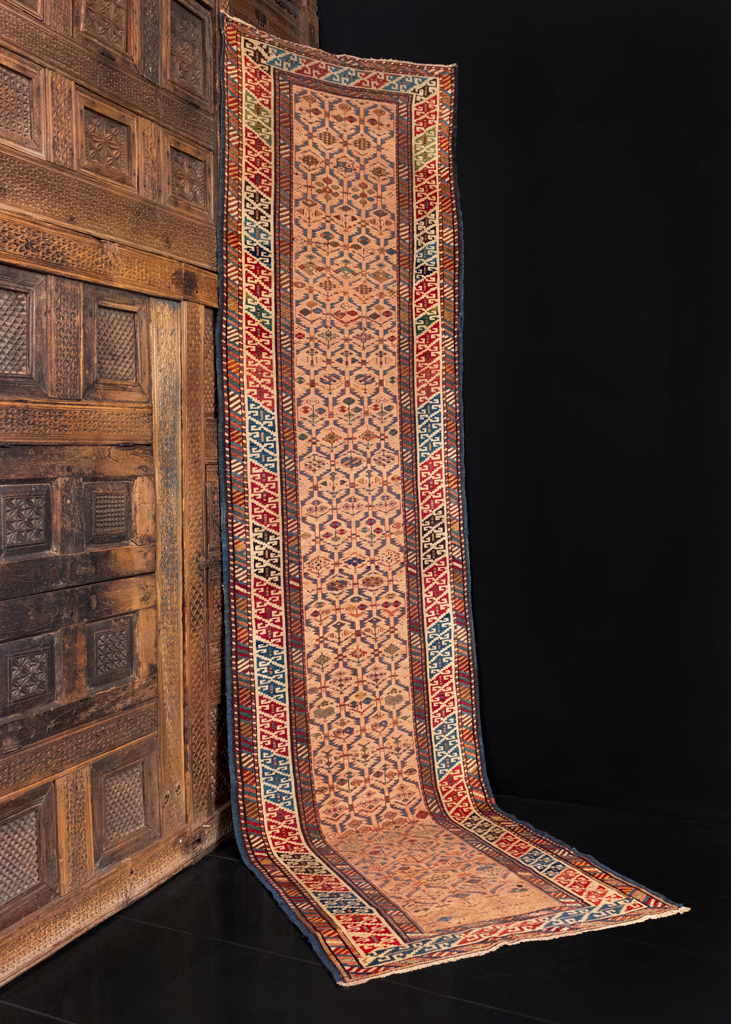 Shrivan runner handwoven in the Eastern Caucasus at the turn of the 20th century. Field is a variation on a lattice design woven in soft blues and yellows on a peach ground. Main border is a double S scroll design on a white ground. 