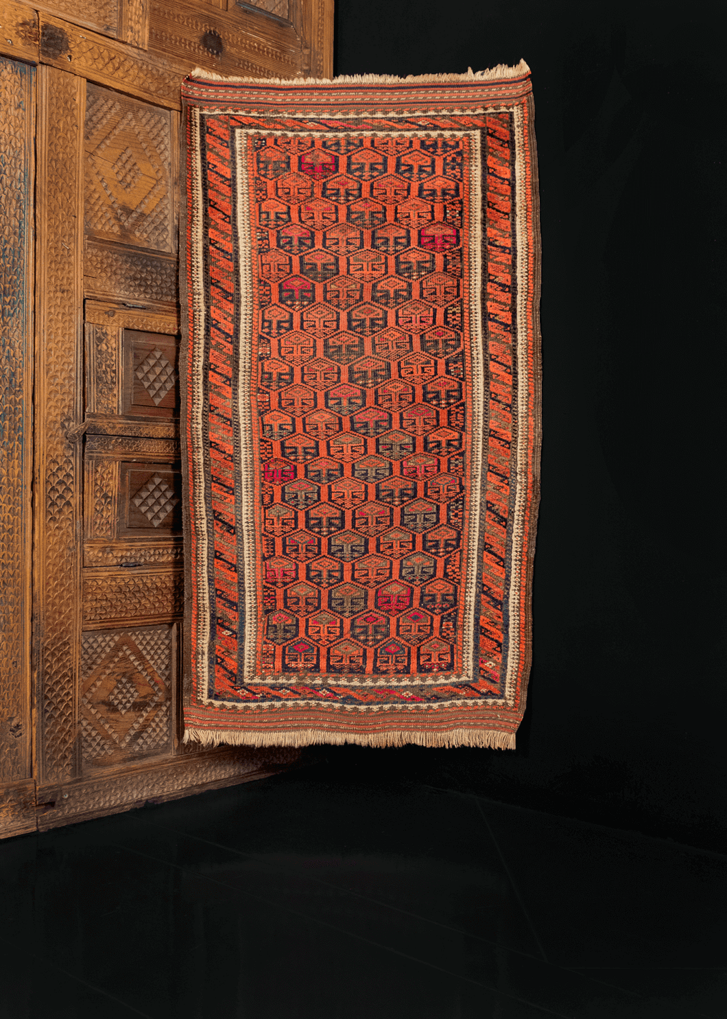 Baluch rug from the second quarter of 20th century with diagonal repeat design in reds, oranges, and browns with pops of fuchsia