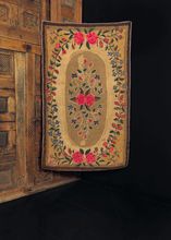 Hook rug made in New England during second quarter of 20th century. Wreath of flowers circling a central floral spray on a taupe ground. Earth tones of field contrast with bright pink of the roses and soft blues of flowers. 