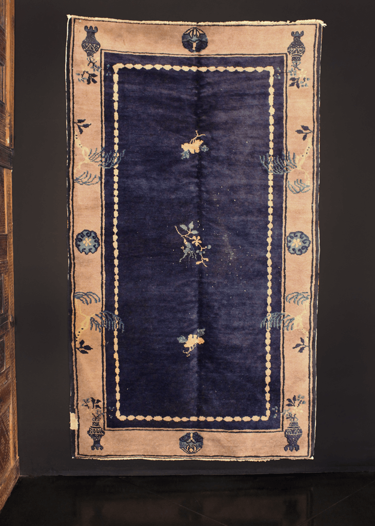 Chinese Peking rug handwoven early 20th century. Deep blue indigo field with minimal central design of flowers. Gray-ivory border with plants and flower vases. 